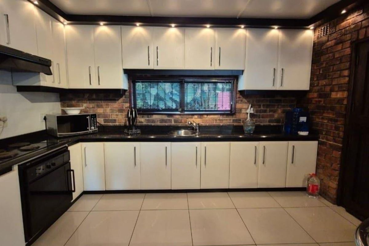 A well-maintained kitchen featuring white cabinetry, black granite countertops, exposed brick accents, and modern recessed lighting.