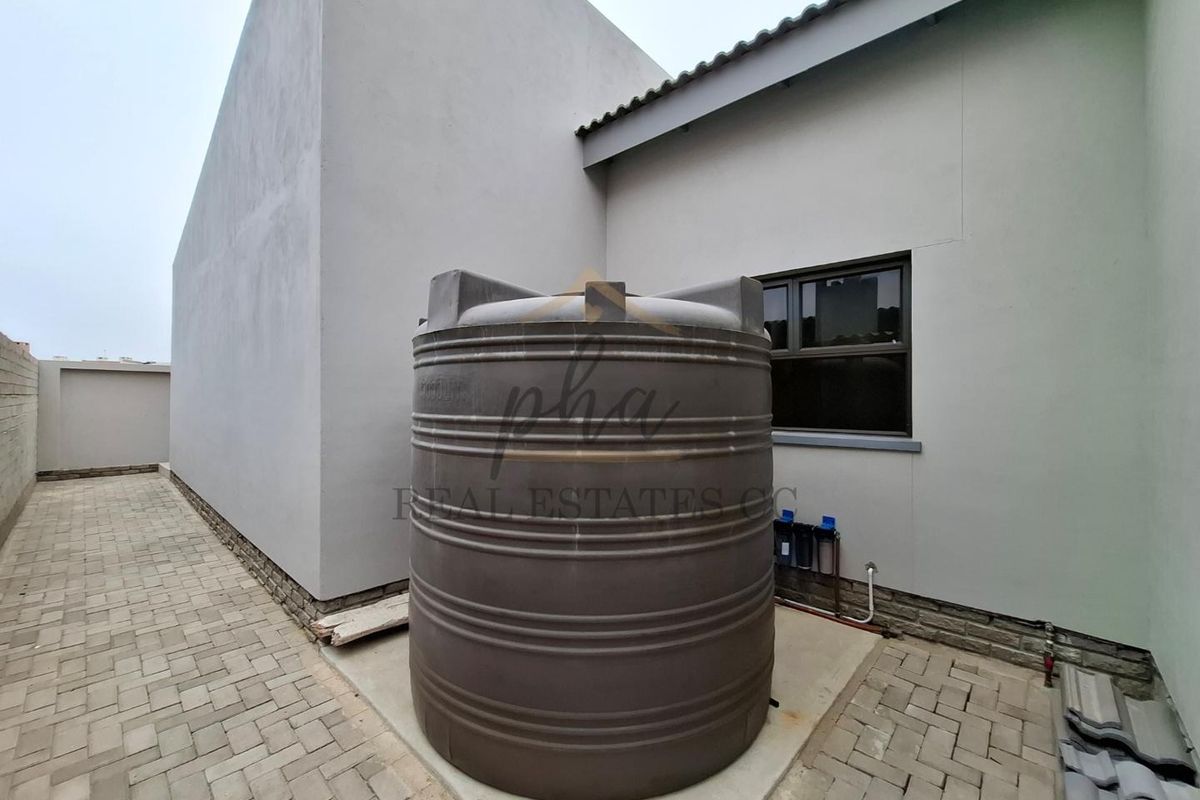 Exterior side area featuring a large water storage tank, paved ground, and a water filtration system mounted on the exterior wall.