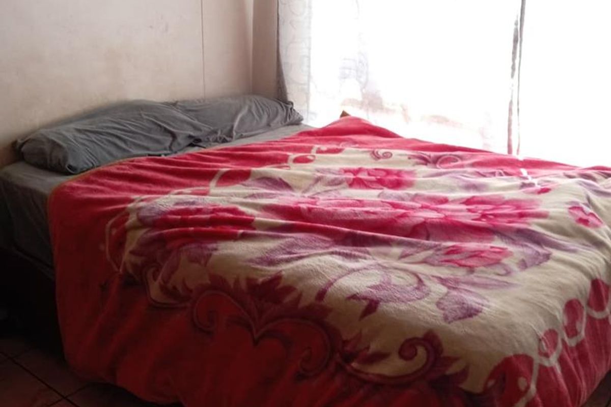 A bedroom featuring tiled flooring and a large window with natural light, providing a simple and functional living space.