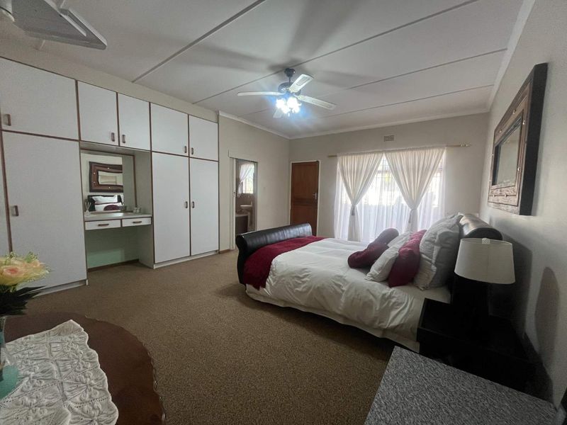 Spacious bedroom featuring extensive built-in cupboards with an integrated vanity, ceiling fan, and carpeted flooring.
