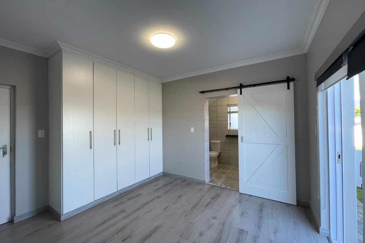 A bright, modern bedroom featuring light-toned laminate flooring, extensive built-in cupboards, and a stylish sliding barn door leading to an en-suite bathroom.