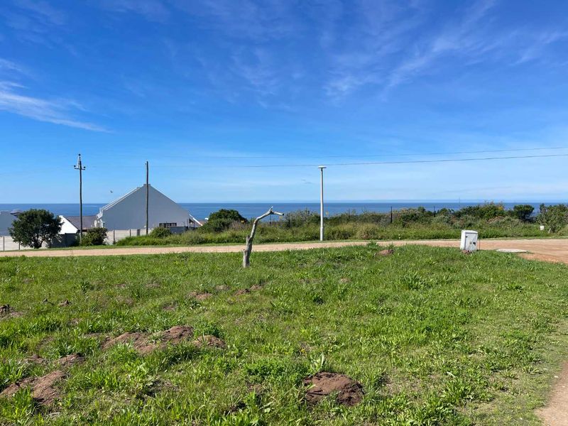 A scenic view overlooking a coastal landscape with open green space, utility infrastructure, and distant ocean horizon.