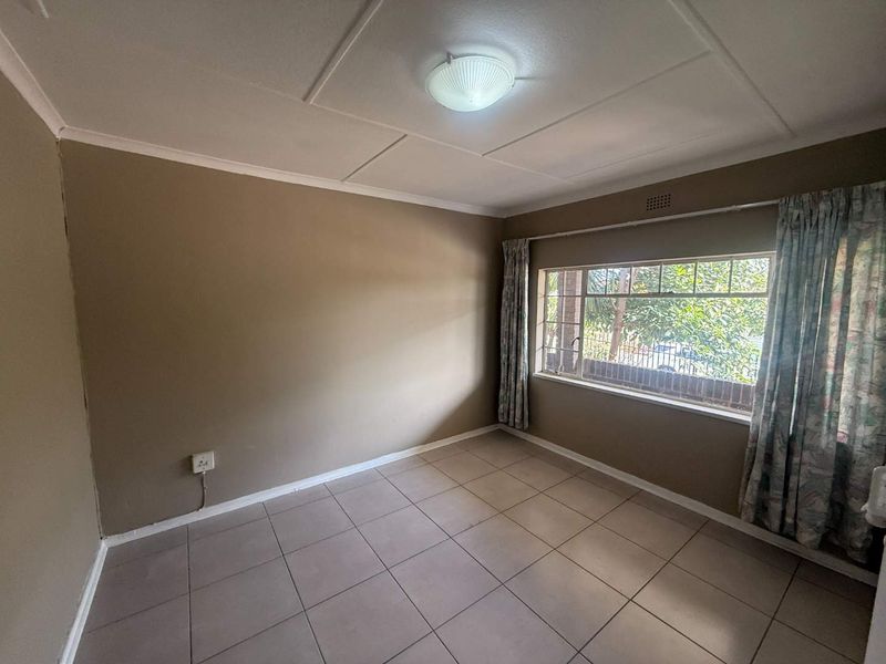 An empty bedroom featuring tiled flooring, a large window providing natural light, and a standard ceiling light fixture.