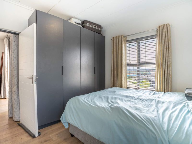 A well-lit bedroom featuring modern dark grey built-in wardrobes, light laminate flooring, and a window with blinds offering natural light.