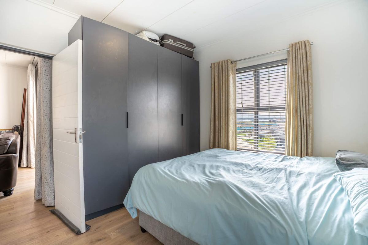 A well-lit bedroom featuring modern dark grey built-in wardrobes, light laminate flooring, and a window with blinds offering natural light.
