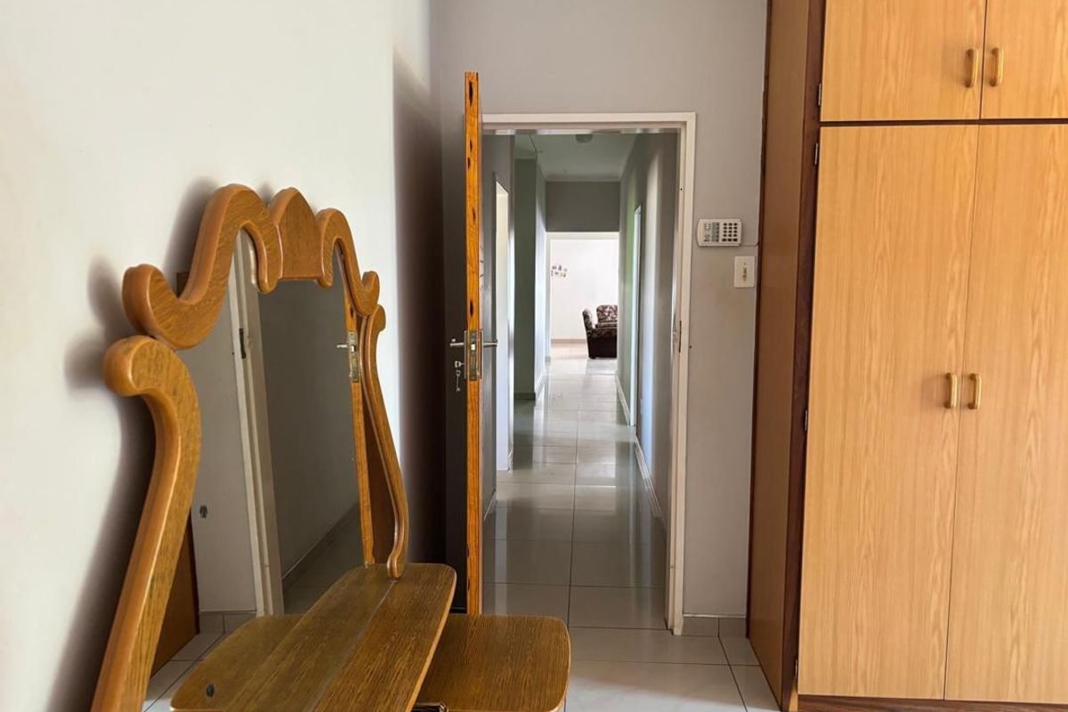 A bedroom featuring built-in wooden cupboards and tiled flooring, with a doorway leading into a central hallway.