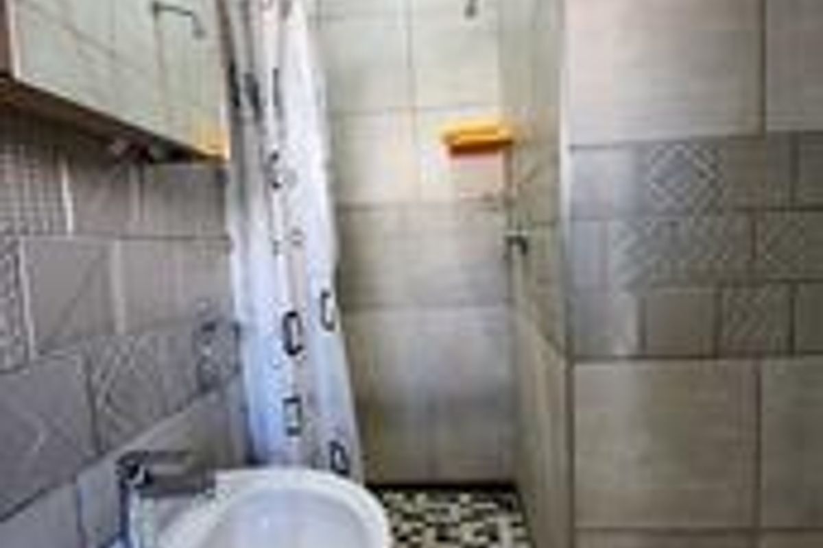 A functional bathroom featuring a pedestal basin, wall-mounted mirror, and a tiled shower enclosure with a shower head.