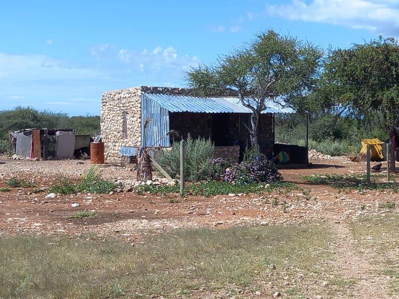 A rustic stone-walled farm structure featuring a corrugated metal roof and a covered porch area set within a rural landscape.