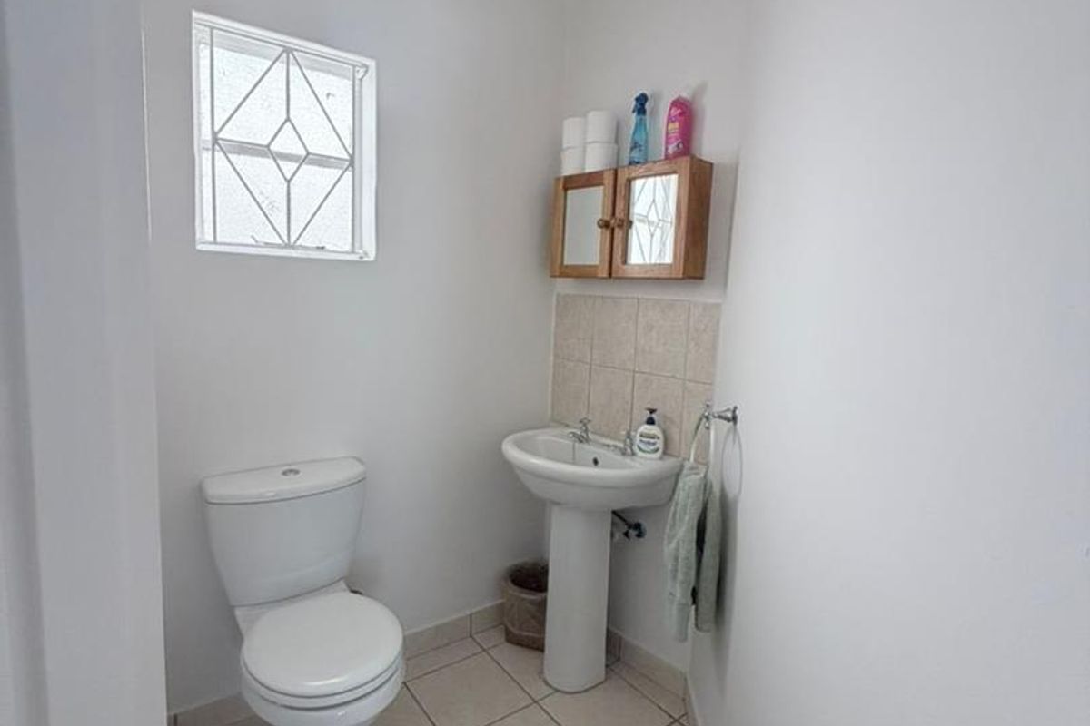 A functional guest bathroom featuring a pedestal basin, toilet, tiled flooring, and a small window with security bars.