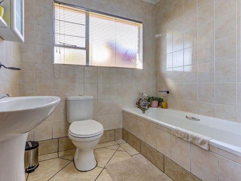 A functional bathroom featuring a pedestal basin, toilet, and bathtub with neutral wall and floor tiling.