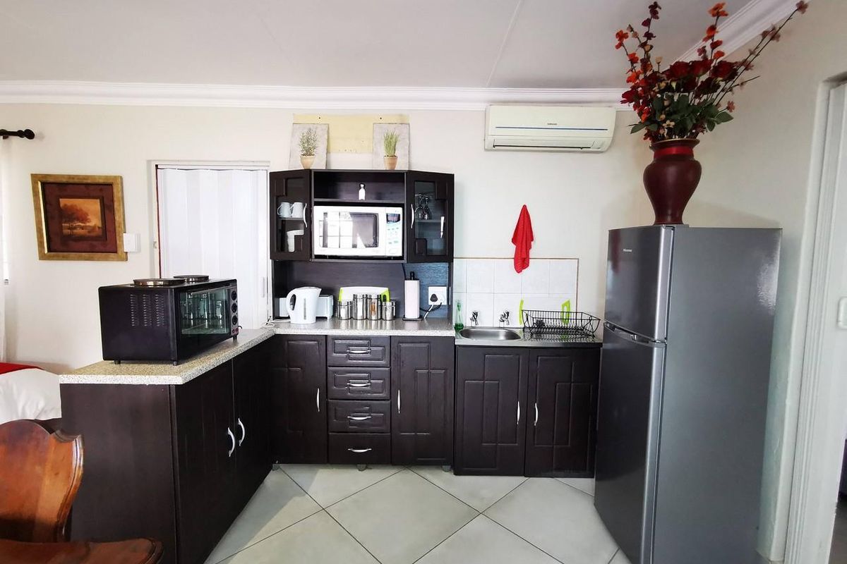 Compact kitchen area featuring dark wood cabinetry, tiled flooring, a built-in microwave shelf, and a wall-mounted air conditioning unit.