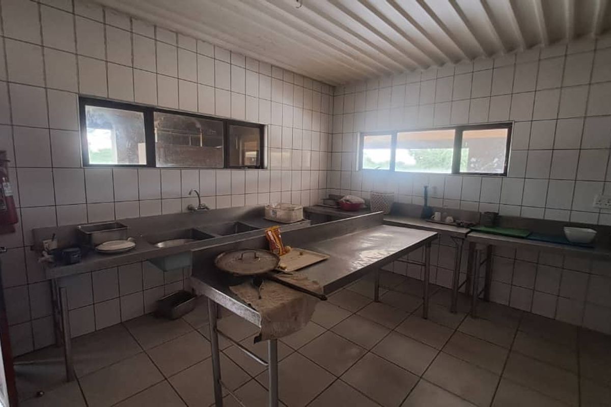 A functional industrial-style kitchen featuring stainless steel prep counters, double sinks, and full-height wall tiling, suitable for high-volume food preparation.