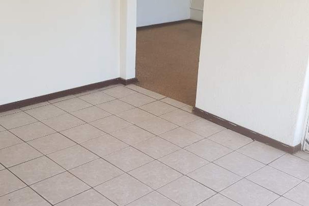 An empty living area featuring neutral ceramic floor tiles and a doorway leading to an adjacent carpeted room.