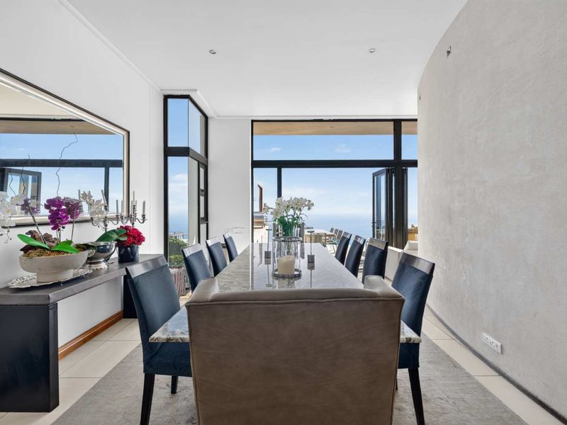 Elegant dining room featuring large format floor tiles, a textured feature wall, and expansive floor-to-ceiling glass doors offering panoramic ocean views.