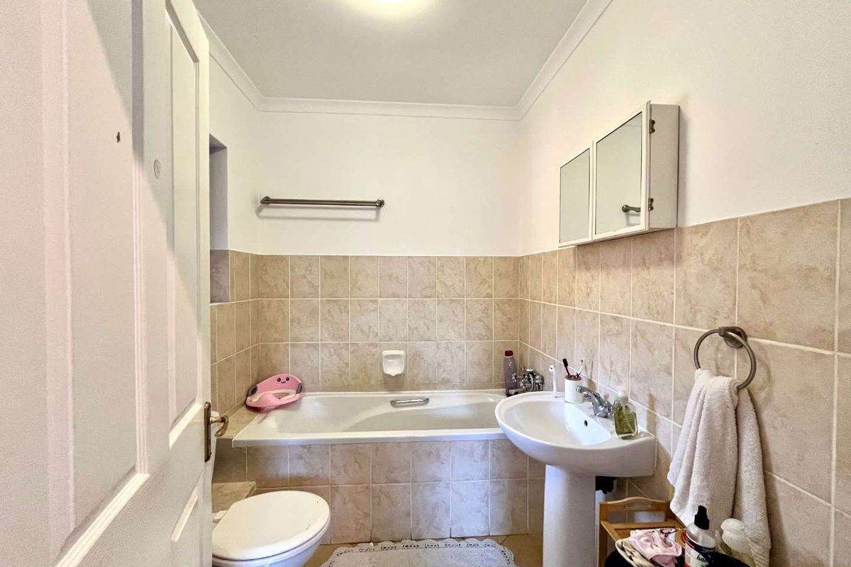 A functional bathroom featuring a bathtub, pedestal sink, toilet, and wall-mounted medicine cabinet with neutral ceramic tiling.