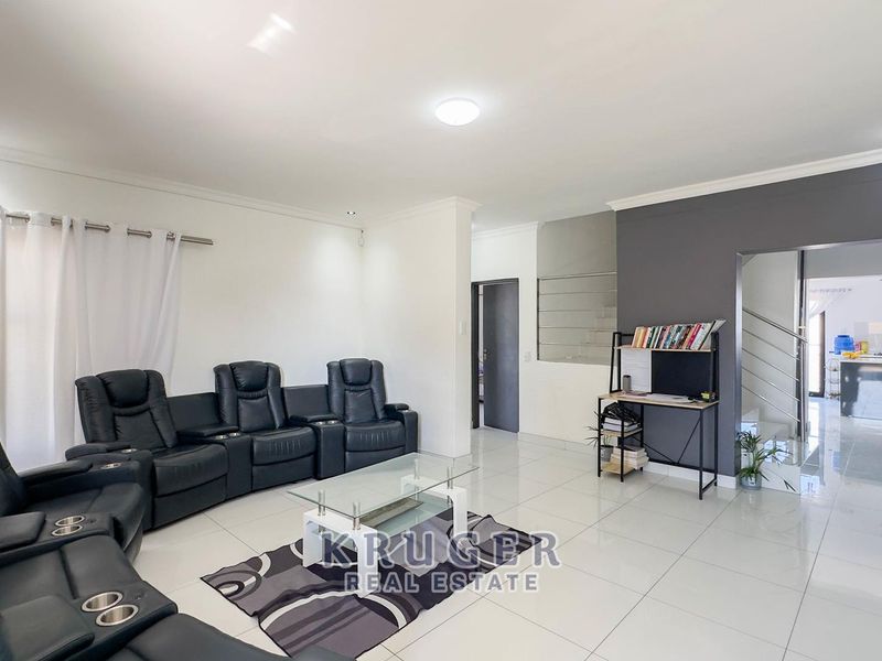 Spacious open-plan living area featuring polished porcelain floor tiles, modern recessed lighting, and a feature wall, seamlessly connecting to the kitchen and staircase.