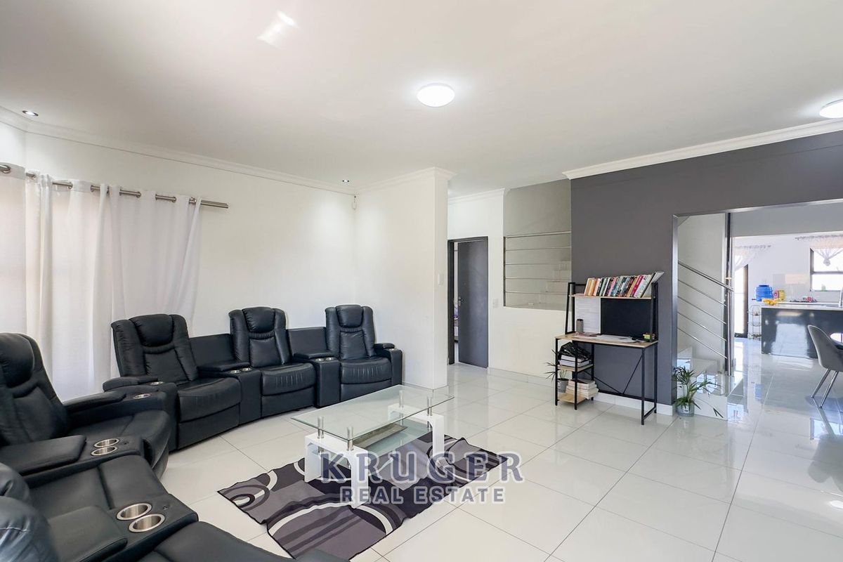 Spacious open-plan living area featuring polished porcelain floor tiles, modern recessed lighting, and a feature wall, seamlessly connecting to the kitchen and staircase.
