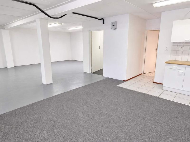 Open plan industrial office or studio space featuring a functional kitchenette, neutral finishes, and a combination of carpeted and tiled flooring.