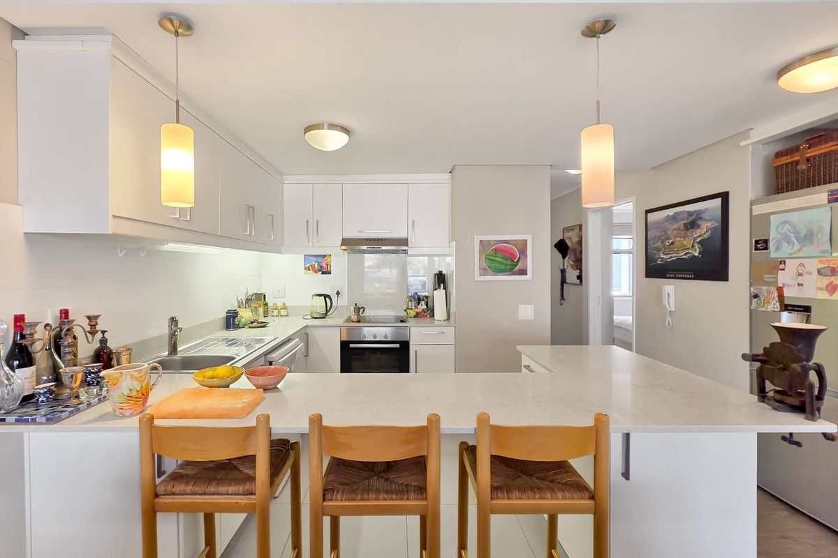 Modern kitchen featuring white cabinetry, stone countertops, a breakfast bar, and integrated appliances, creating a functional and bright open-plan cooking space.