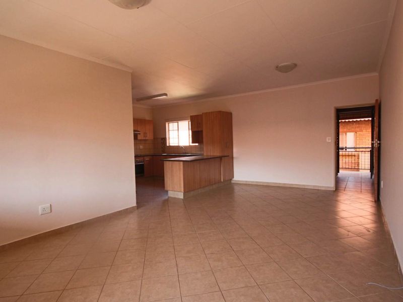 An open-plan living and kitchen area featuring tiled flooring, built-in wooden cabinetry, a breakfast bar, and integrated kitchen appliances.