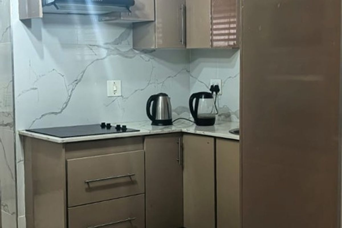 A compact, modern kitchen featuring sleek cabinetry, marble-look splashbacks, an integrated electric hob with extractor fan, and stylish pendant lighting.