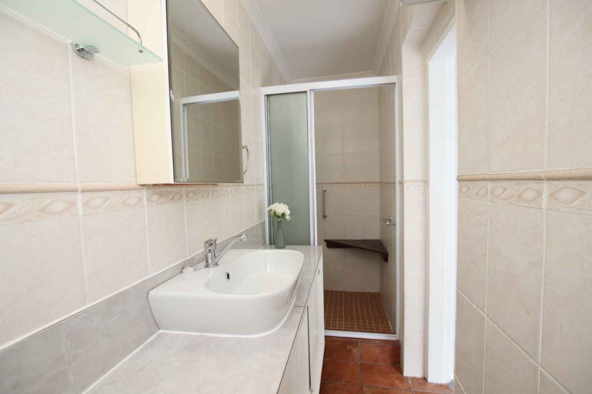 A functional bathroom featuring a vanity with a basin, a walk-in shower with a built-in seat, and neutral wall tiling.