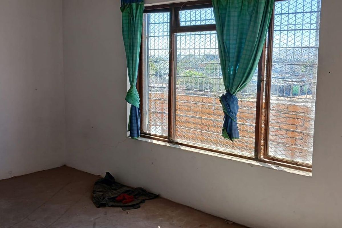 An empty room featuring a large window with security bars, providing natural light and a view of the surrounding area.