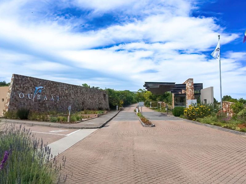 The entrance to Oubaai estate featuring a stone-clad boundary wall, paved driveway, and professional landscaping.