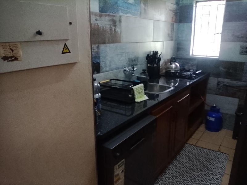 A functional kitchen featuring dark granite countertops, built-in cabinetry, a gas hob, and decorative tiled splashbacks with a window for natural light.