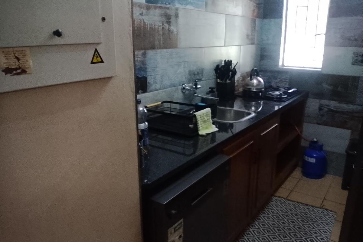A functional kitchen featuring dark granite countertops, built-in cabinetry, a gas hob, and decorative tiled splashbacks with a window for natural light.