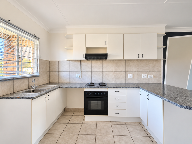 A clean, functional kitchen featuring white cabinetry, granite countertops, a built-in oven with hob, and neutral tiled flooring and backsplash.