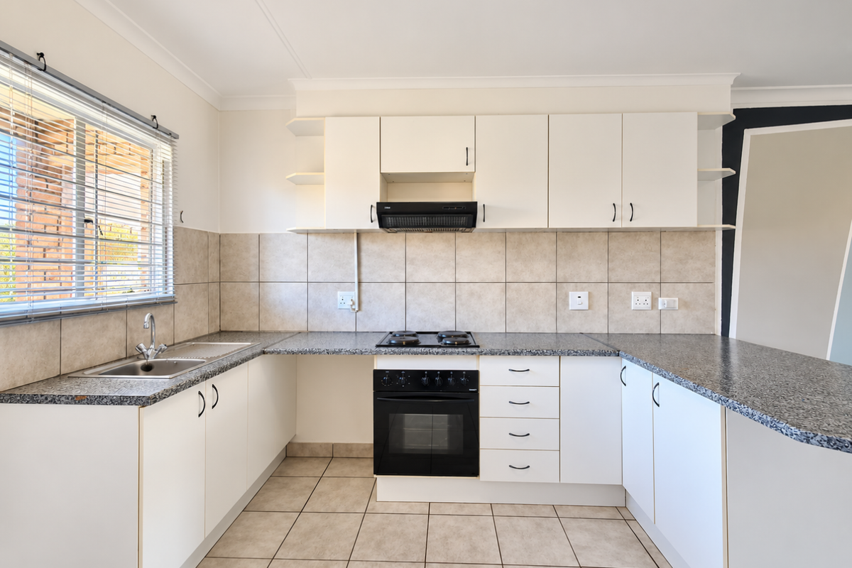 A clean, functional kitchen featuring white cabinetry, granite countertops, a built-in oven with hob, and neutral tiled flooring and backsplash.