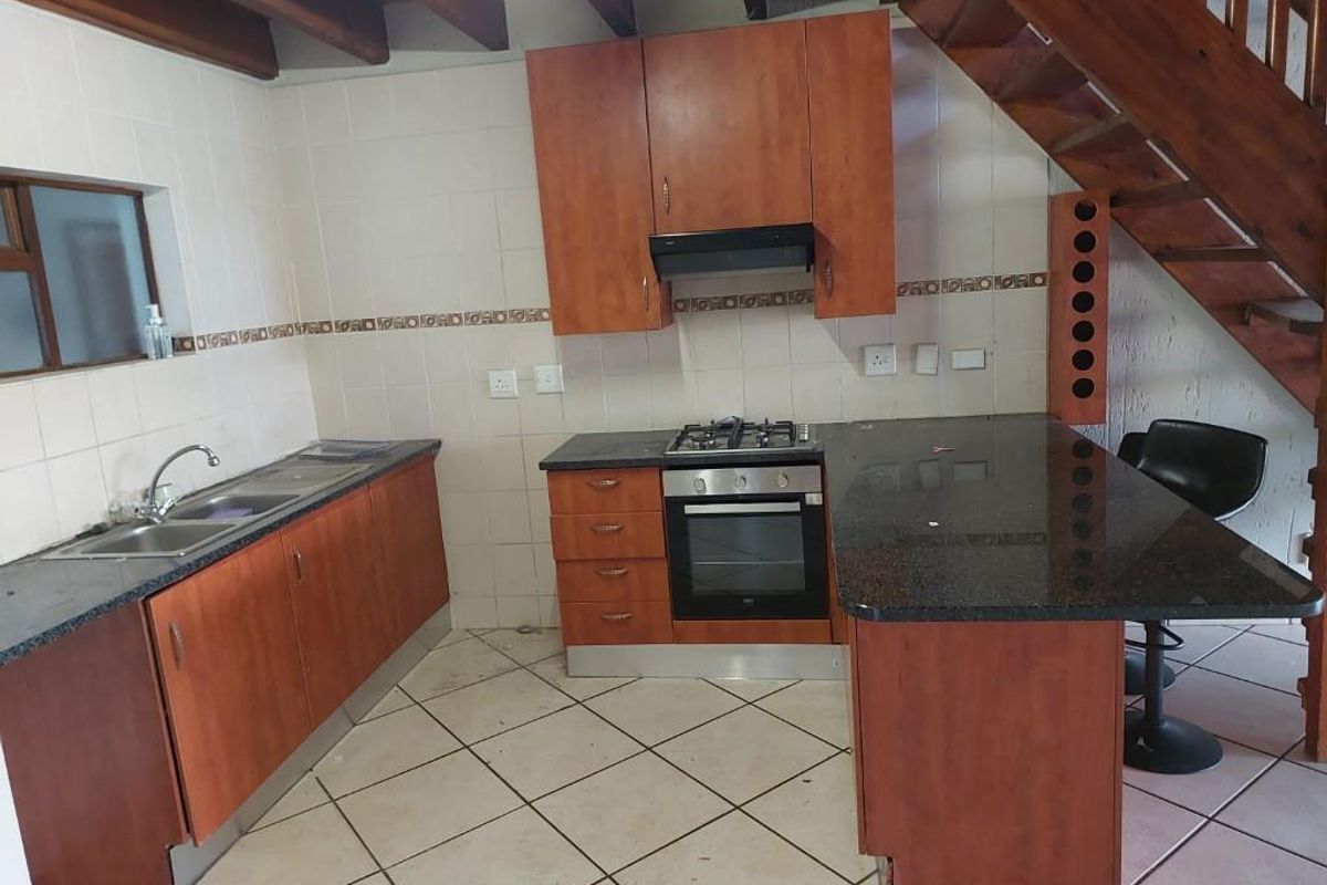 Kitchen featuring wooden cabinetry, granite countertops, built-in oven and gas hob, with an adjacent wooden staircase and tiled flooring.