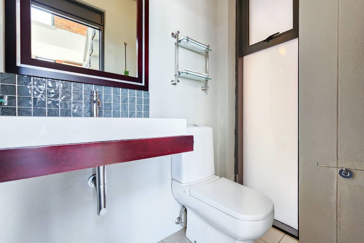A modern bathroom featuring a wall-mounted vanity with a basin, tiled splashback, framed mirror, and a toilet with a frosted glass window.