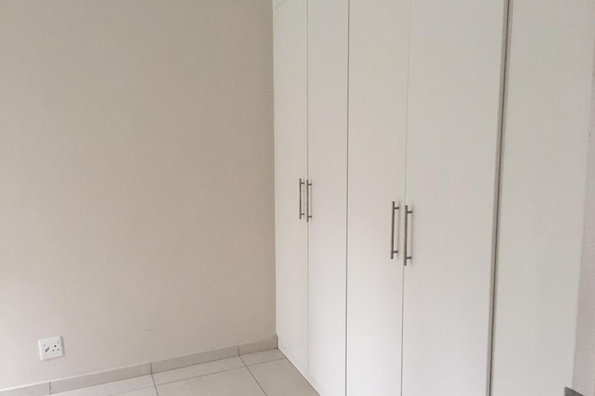 A clean, empty bedroom featuring neutral walls, tiled flooring, and ample built-in cupboard storage.