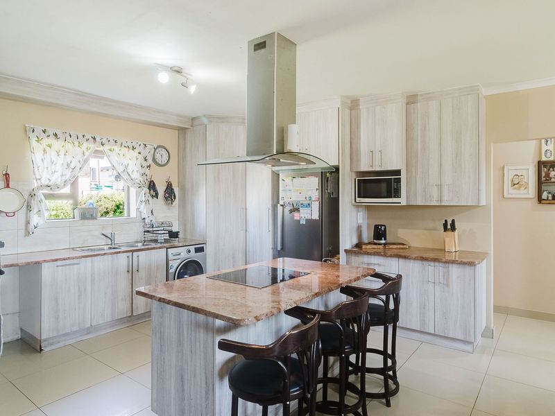 A functional kitchen featuring light wood-grain cabinetry, granite countertops, a central island with a hob, and integrated appliances.