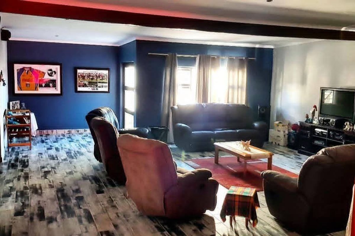 Spacious living room featuring dark blue accent walls, recessed ceiling lighting, and distinctive wood-look tiled flooring.