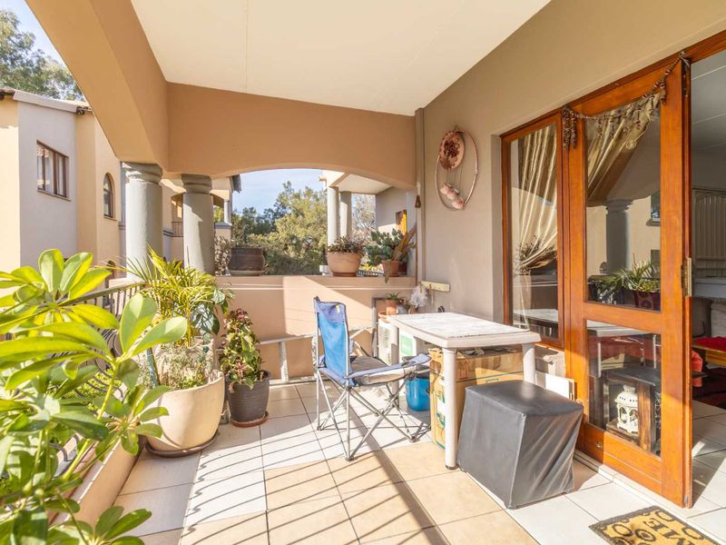 A covered balcony featuring tiled flooring, concrete columns, and a wooden sliding door providing access to the interior living space.