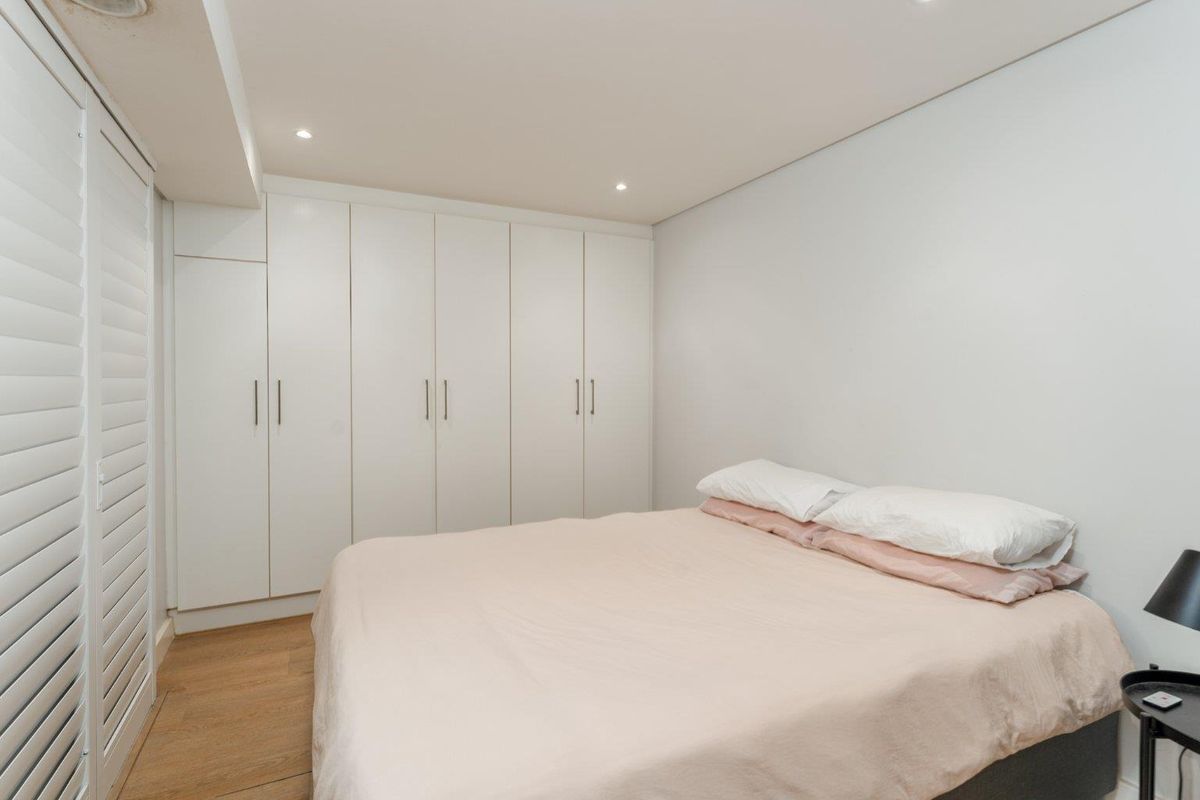 A clean and modern bedroom featuring extensive built-in floor-to-ceiling cupboards, recessed downlighting, and warm timber flooring.