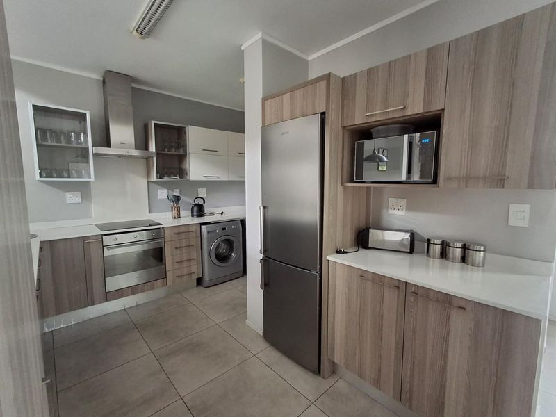Modern kitchen featuring wood-finish cabinetry, stone countertops, integrated stainless steel appliances, and tiled flooring with dedicated space for laundry appliances.