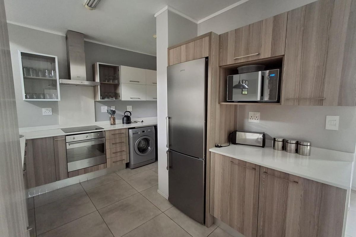 Modern kitchen featuring wood-finish cabinetry, stone countertops, integrated stainless steel appliances, and tiled flooring with dedicated space for laundry appliances.