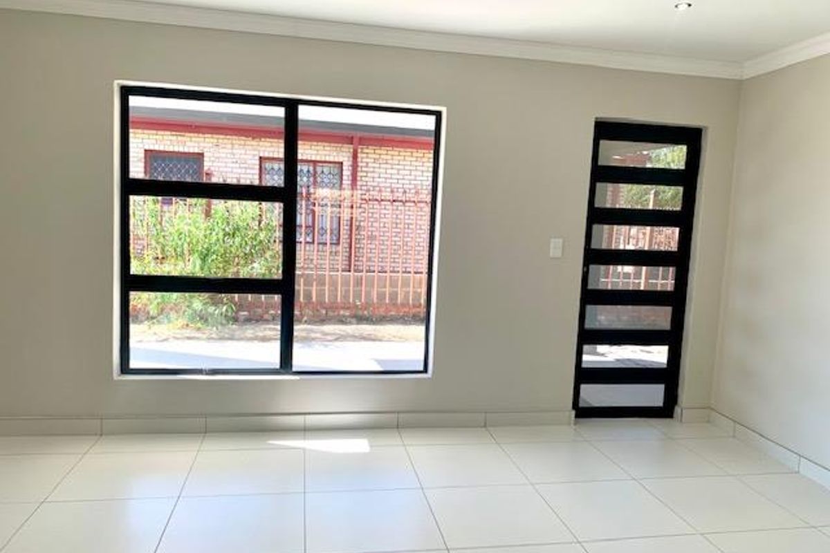 A bright, empty living area featuring neutral tiled flooring, modern recessed lighting, and a contemporary black-framed door and window.