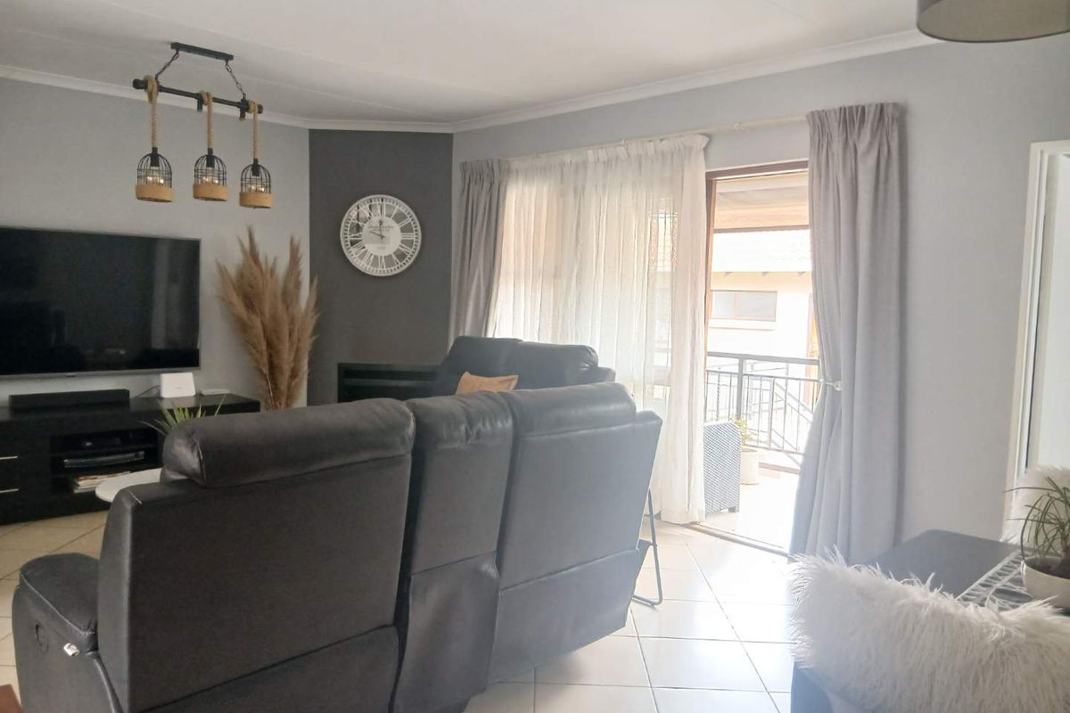 A bright living room featuring tiled flooring, modern pendant lighting, and a sliding glass door providing access to an outdoor balcony area.