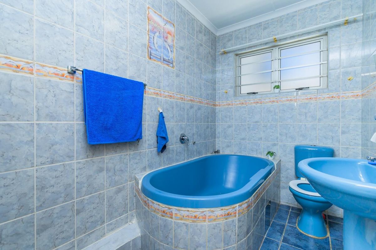 A functional bathroom featuring a built-in bathtub, pedestal sink, and toilet, finished with blue tiled walls and flooring.