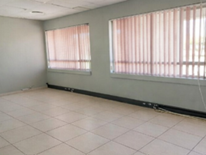 An empty office space featuring tiled flooring, suspended ceiling tiles, and large windows with vertical blinds.