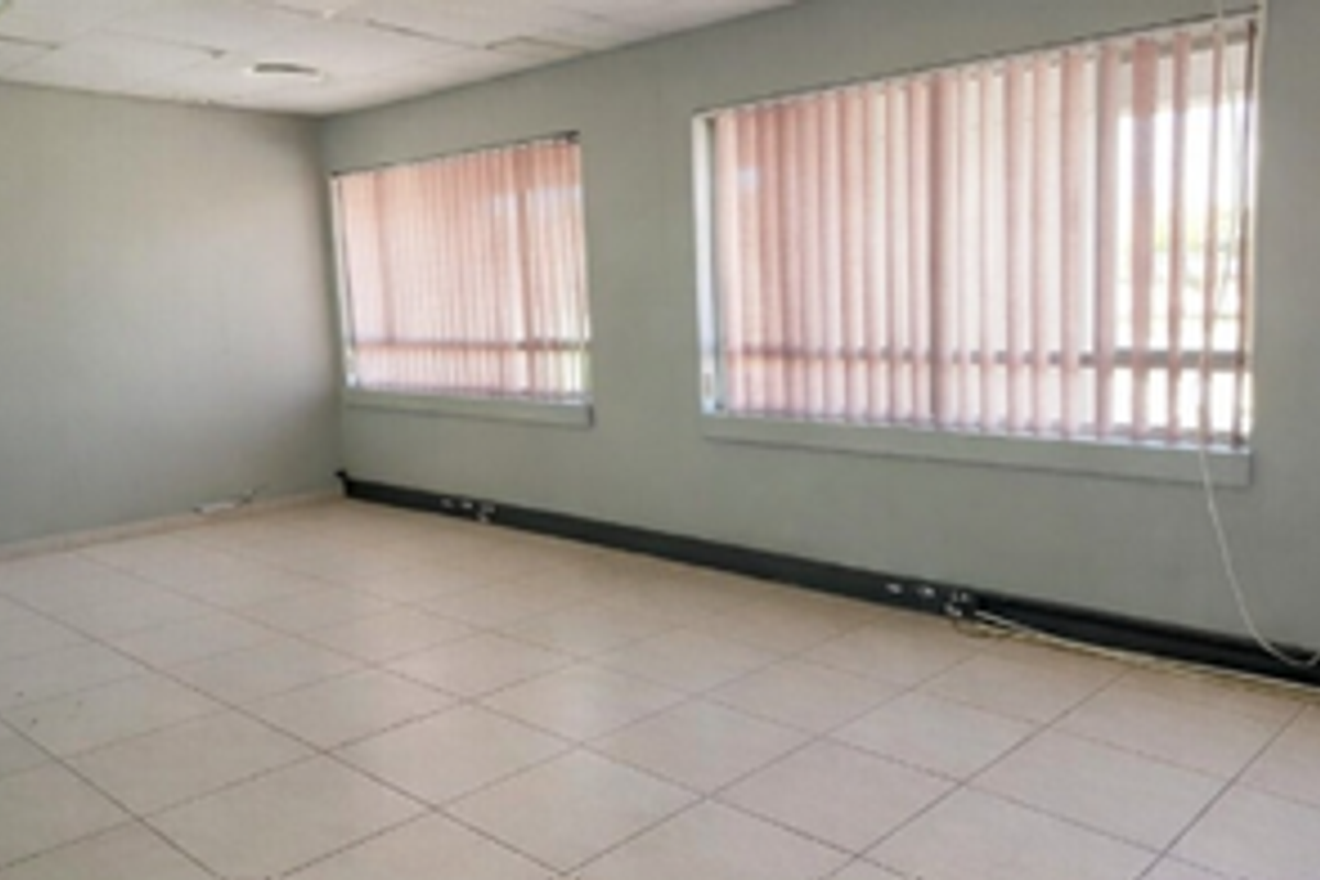 An empty office space featuring tiled flooring, suspended ceiling tiles, and large windows with vertical blinds.