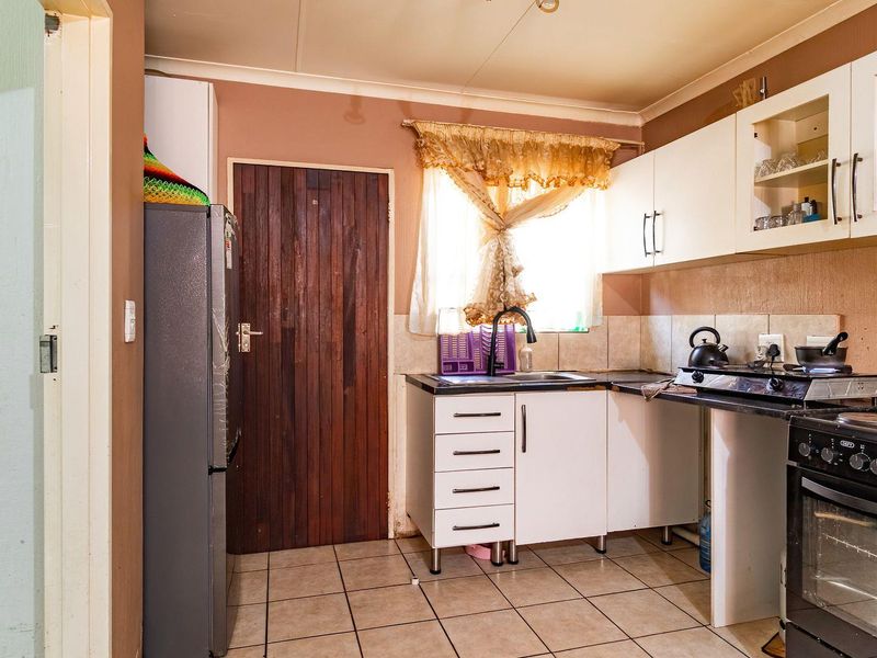 A compact kitchen featuring white cabinetry, tiled flooring, a tiled splashback, and a freestanding oven, offering a functional layout with potential for modernization.