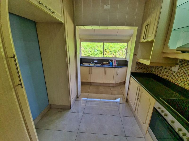 A functional kitchen featuring built-in cabinetry, granite countertops, mosaic tile backsplash, and tiled flooring, with a view through to a secondary prep area.