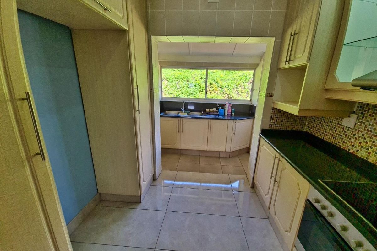 A functional kitchen featuring built-in cabinetry, granite countertops, mosaic tile backsplash, and tiled flooring, with a view through to a secondary prep area.