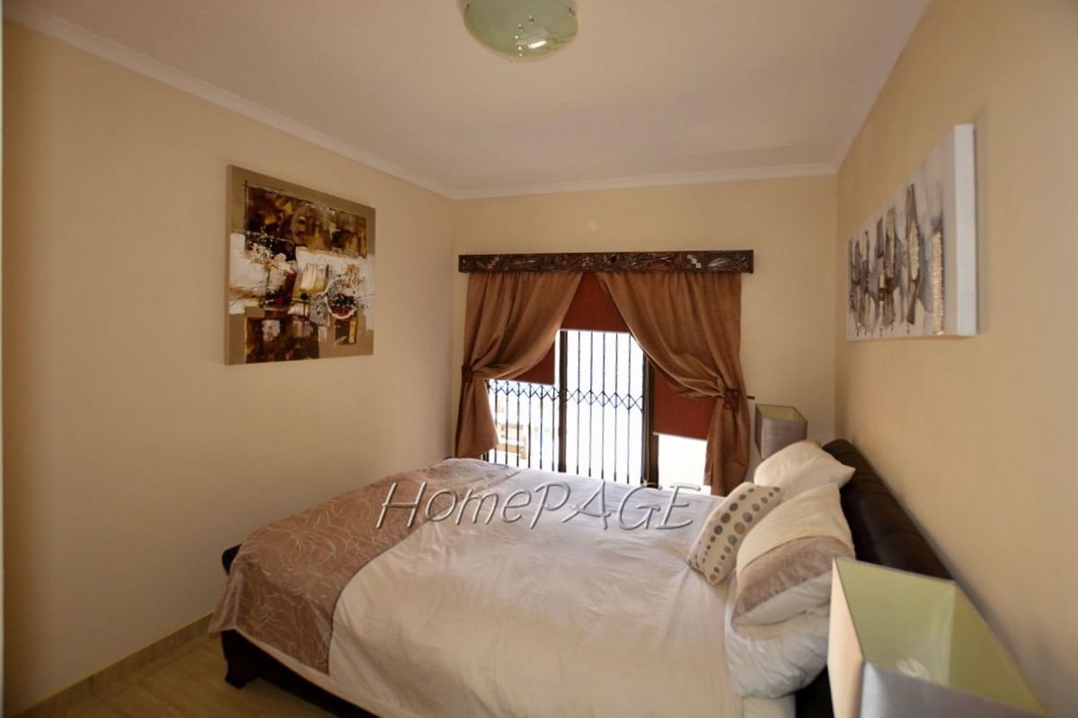 A cozy bedroom featuring neutral wall tones, tiled flooring, and a window fitted with security bars and a decorative pelmet.